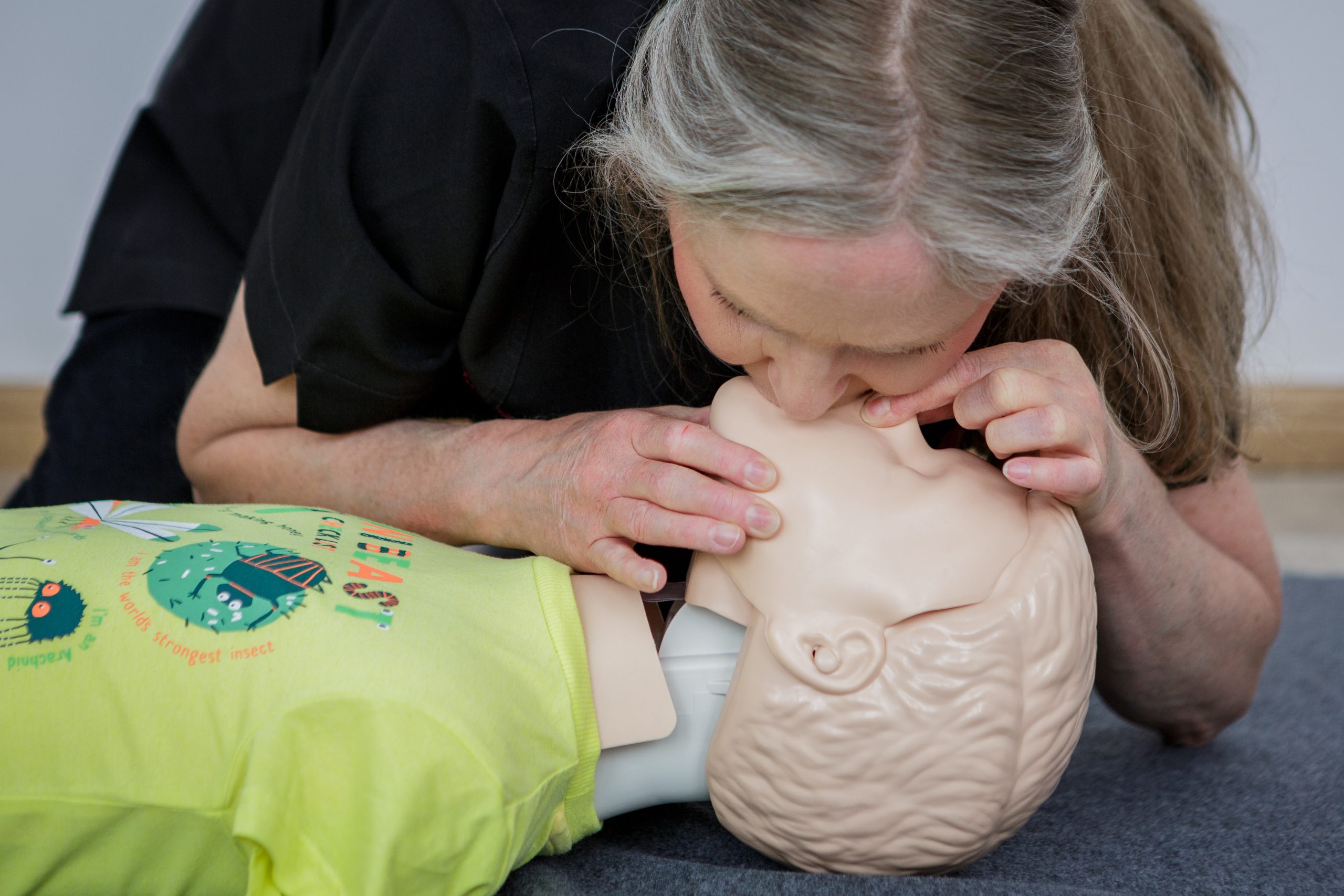 Karen carrying out rescue breaths on a child manikin for child first aid. The child manikin is wearing a yellow t-shirt.