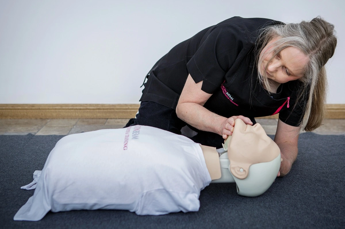Karen in black uniform, tilting the adult CPR manikin's head back to check for breathing during first aid training