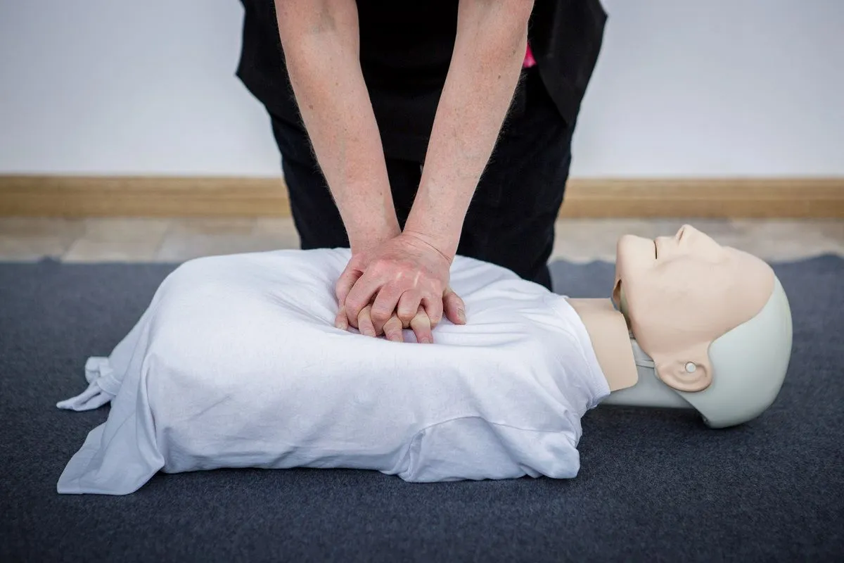 CPR being carried out on an adult manikin wearing a white t-shirt, for first aid training.